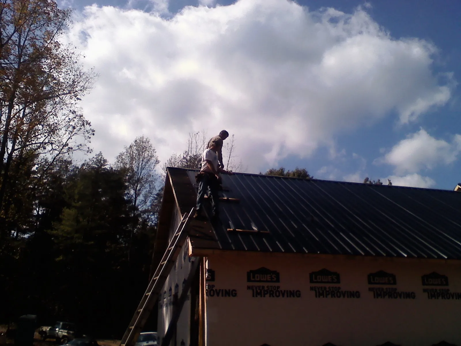 Roofer fastening dark metal panels high against a cloudy sky, from a Roof Inspection job in Brookline