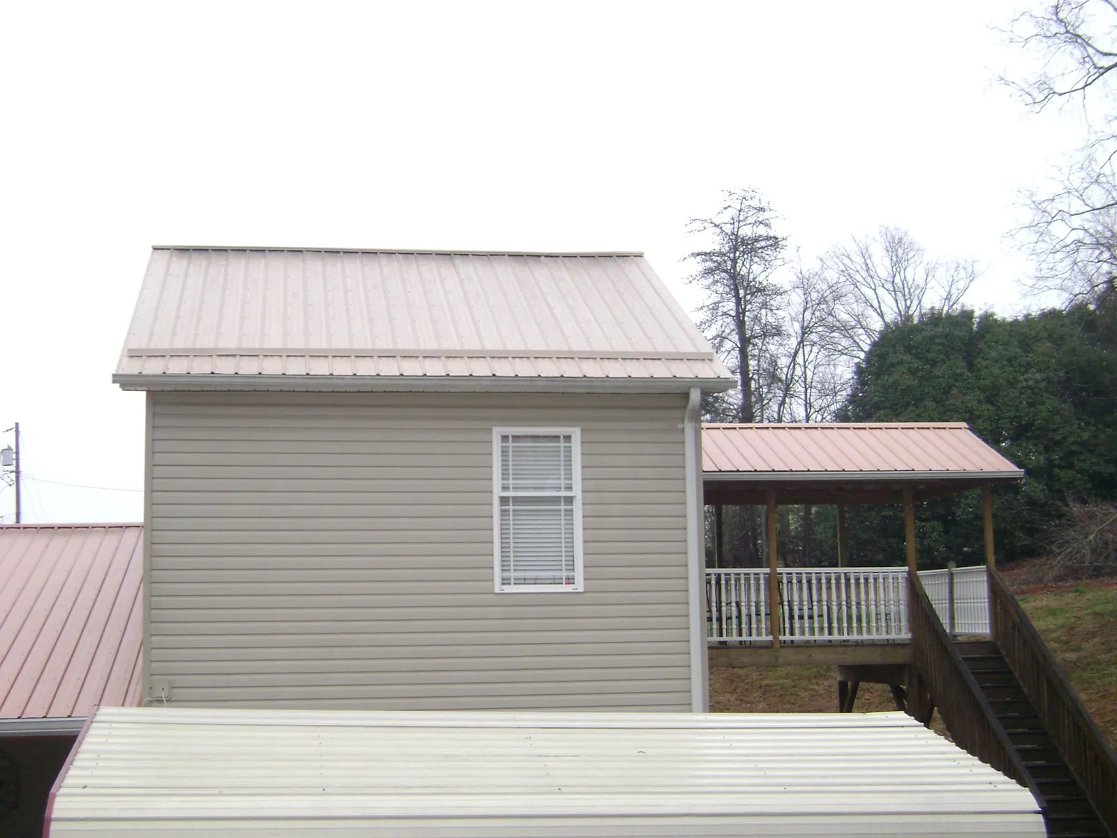 Tan metal roofs on a two story addition and attached porch, from a Roof Replacement job in Brookline